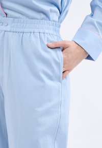 Světle modré bavlněné kalhoty s elastickým páskem, které mají postranní kapsu a hladkou strukturu. Růžové švy zdobí design.