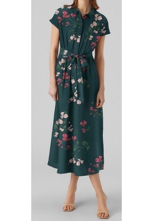 Femme portant une robe midi vert foncé avec des motifs floraux roses et blancs, manches courtes, col boutonné et ceinture nouée à la taille.