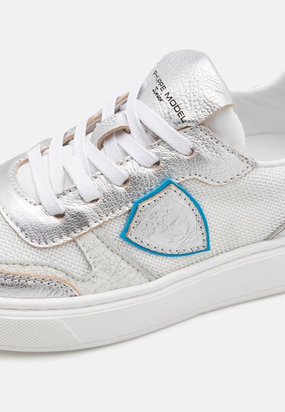 Silberne Leder-Sneaker mit weißen Textilakzenten, blauen Details, weißen Schnürsenkeln, strukturierten Oberflächen und gepolstertem Knöchelkragen.