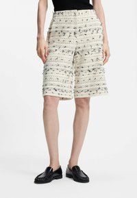 Shorts crème avec un motif parsemé noir, en tissu tissé texturé, taille élastique et coupe mi-genou. Chaussures noires à enfiler.