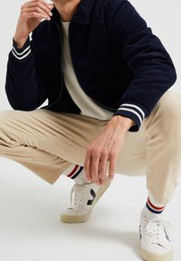 Marinblå kordjacka med vita randiga manschetter, beige kordbyxor och vita sneakers med svarta detaljer. Texturerade tygdetaljer synliga.