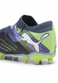 Nogometne kopačke s gornjim dijelom od tamnoplavog mrežastog materijala, zelenim i crnim prugama, ljubičastim naglaskom i bijelim Puma logom sa strane.