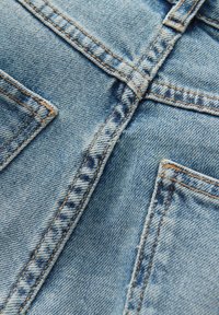Lichtblauwe denimstof met contrasterende gele stiksels, met een gladde textuur en zichtbare naden, inclusief bovenste zakken en een knopenlijst.
