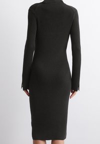 Robe côtelée vert foncé avec des manches longues, silhouette ajustée et fentes sur les côtés. Présente un col haut et un tissu texturé.