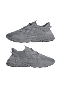 Sneaker sportive grigie con tomaia in rete, dettagli testurizzati, forme dinamiche e una suola in gomma spessa con un motivo ondulato.