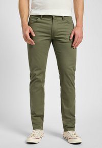 Pantalones de algodón elástico verde oliva con cinco bolsillos, diseño ajustado, costuras sutiles, y combinados con zapatillas de lona beige.