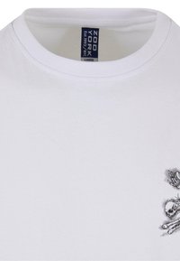 Hvid bomulds T-shirt med rund hals, korte ærmer og et sort grafisk design af et kranium med vinger på venstre bryst.