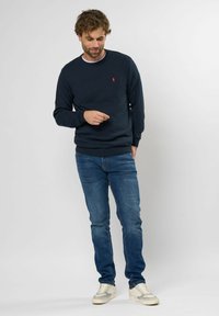 Marine crewneck sweatshirt met ribgebreide halslijn en manchetten, gecombineerd met blauwe jeans en lichte sneakers; heeft een subtiele logodetail op de borst.