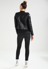 Sort læderjakke med en tætsiddende pasform og skulderepauleter, parret med sorte skinny jeans og sølvfarvede ankelstøvler.