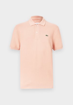 Polo shirt piersica deschisă din bumbac, cu un guler clasic, mâneci scurte, placket cu trei butoane și un logo brodat verde.