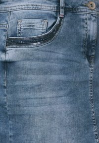 Jeans i denim i ljusblått med en något blekt struktur. Har en frontficka med mörk kant och en metallknapp som stänger.