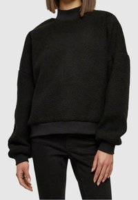 Pullover in pile nero con collo alto, forma oversize e orlo e polsini elasticizzati. Superficie strutturata con un aspetto morbido e caldo.