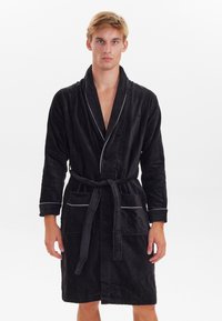 Accappatoio in cotone nero con colletto a scialle, vita con cintura e piping bianco. Presenta due tasche frontali e maniche lunghe con polsini.