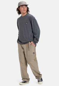Long-sleeve gray striped shirt with a logo patch, paired with beige cargo pants and black sneakers, worn with a gray cap.