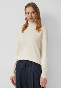 Maglione a collo alto beige chiaro, tessuto lavorato a maglia, vestibilità comoda, con maniche lunghe. Abbinato a pantaloni scuri a righe sottili.