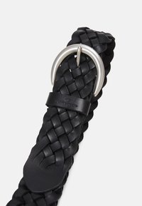 Cinturón de cuero trenzado negro con hebilla de metal de tono plateado y un lazo de cuero liso para asegurar el extremo del cinturón.
