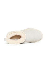 Stivaletto in suede grigio con una morbida fodera in pelliccia crema e una suola in gomma beige a contrasto. Presenta un comodo inserto sul retro per facilitare la calzata.