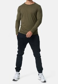 Olijfgroene langemouwen shirt met ronde hals en textuurstof, gecombineerd met marineblauwe joggingsbroek, afgemaakt met witte sportschoenen.
