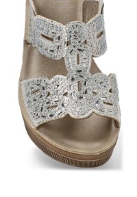 Sandalía de cuña beige con un interior texturizado brillante, que presenta una correa adornada en plata con intrincados recortes y acentos de cuentas brillantes.
