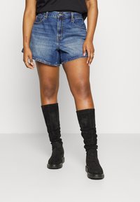 Szorty dżinsowe w średnim odcieniu niebieskiego z podwiniętymi nogawkami, zestawione z czarnymi, luźnymi kozakami do kolan. Strój uzupełnia prosty czarny top.