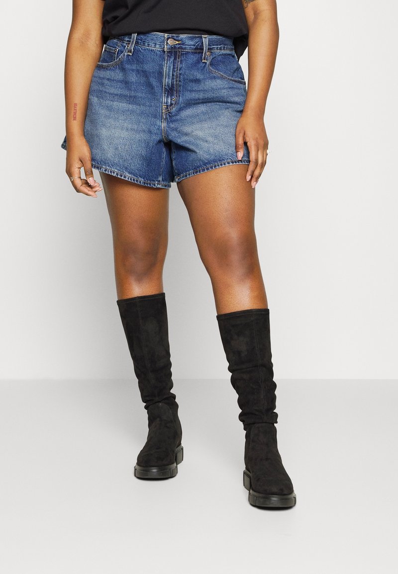 Szorty dżinsowe w średnim odcieniu niebieskiego z podwiniętymi nogawkami, zestawione z czarnymi, luźnymi kozakami do kolan. Strój uzupełnia prosty czarny top.