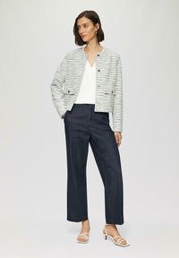 Lightly textured, multicolored tweed jacket with gold buttons, paired with dark, wide-leg denim trousers and white strappy heels.