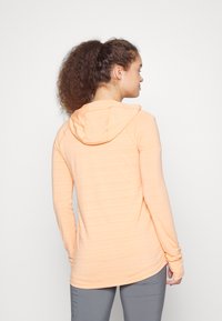 Hoodie de mangas longas em laranja claro com acabamento texturizado e capuz com cordão. Apresenta buracos para os polegares nas mangas e uma bainha curva.