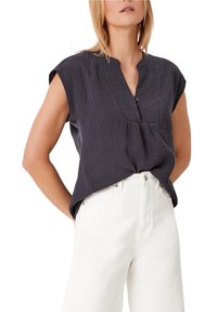 Chemise courte à manches courtes de couleur gris foncé, avec un col à boutons, en tissu texturé et une coupe décontractée, associée à un jean blanc taille haute.