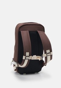 Brauner Rucksack aus gepolstertem Material, atmungsaktivem Mesh-Rücken, verstellbaren Schultergurten und cremefarbigen Akzenten für Unterstützung und Komfort.