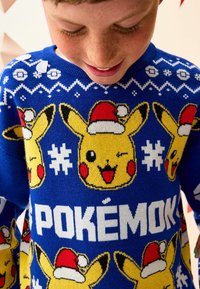 Niebieski sweter z dzianiny z motywami Pikachu w czapkach Mikołaja, płatki śniegu oraz słowo "POKÉMON" w pogrubionym białym tekście na przodzie.