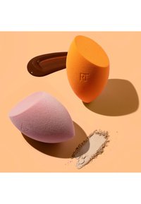 Two makeup sponges, one orange and one pink, with foundation liquid and loose powder on a beige surface.