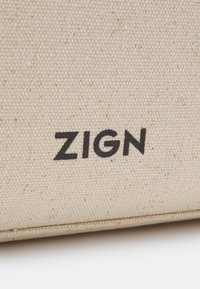 Gros plan d’un tissu beige texturé avec un texte noir "ZIGN" imprimé dessus.