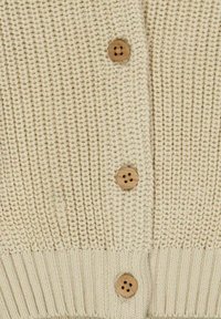 Bežový pletený kardigan s vroubkovaným lemem a strukturovaným tělem, který má čtyři dřevěné knoflíky vpředu pro zapínání.