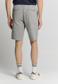 Gray patterned shorts with a relaxed fit and two back pockets, paired with striped socks and light sneakers. The material appears textured.