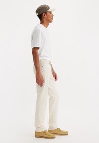 Lichtgekleurde katoenen T-shirt gecombineerd met off-white jeans en tan suede schoenen, accentueel met een grijs en witte pet zijwaarts gedragen.