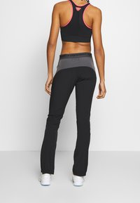 Black athletic pants with a fitted design feature a gray waistband, paired with a black tank top with pink accents and mesh detail.