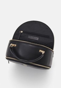 Schwarze runde Handtasche aus Leder mit goldenen Reißverschlüssen und Beschlägen. Das Innere ist mit einem schwarzen gemusterten Futter und einer Reißverschlusstasche ausgestattet.