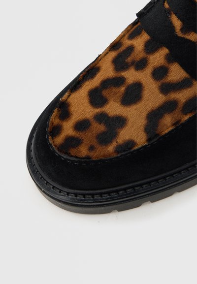 Μαύρο σουέντ παπούτσι με επάνω μέρος σε σχέδιο λεοπάρ με καφέ και σκούρες καφέ κηλίδες. Στρογγυλερή μύτη και υφασμένο λαστιχένιο πέλμα με λεπτομέρειες ραφής.