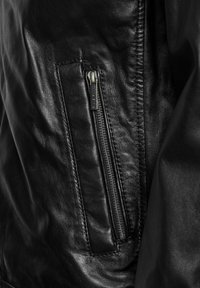 Zwarte leren jack met een ritszak, een gladde textuur en zichtbare stikseldetails. De rits heeft een metalen afwerking.