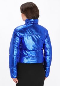 Skinnende blå pufferjakke med h�øj krave og elastiske manchetter, der har en quiltet struktur og en cropped design.