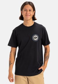 Camiseta de algodón negra con un logo circular impreso en el lado izquierdo del pecho, mangas cortas, cuello redondo y un corte relajado.
