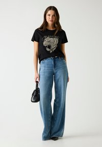 Zwarte graphic t-shirt met een tijgerontwerp, gecombineerd met lichtblauwe wijde jeans. Geaccessoireerd met een kleine zwarte handtas.