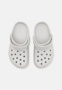 Bílé crocsy s perforovaným designem, texturovanou stélkou a páskem pro pevné uchycení. Vyrobené z lehkého, pružného materiálu.