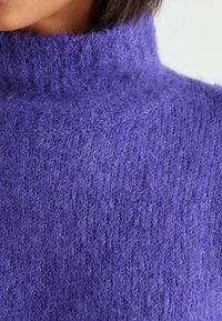 Paarse gebreide trui met een hoge hals, met een zachte, pluizige textuur en een losse weving, met een rijke, diepe kleur.