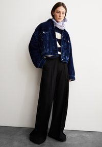 Cropped navy corduroy jacket, buttoned at front, paired with wide black trousers. Underlayer features cream and navy striped sweater, light scarf.