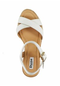 White strappy sandal with cross-over straps and a brown insole. Buckle closure on the ankle, featuring textured detailing. Brand label visible.