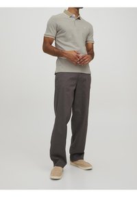 Jasnoszary polo z kontrastowym kołnierzykiem, w zestawieniu z ciemnoszarymi spodniami i beżowymi butami typu slip-on, noszony przez stojącą osobę.