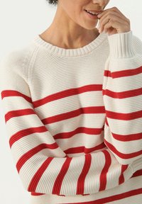 Kremowy sweter z dzianiny z wyrazistymi czerwonymi poziomymi paskami, prążkowanym okrągłym dekoltem i teksturowanym materiałem w luźnym kroju.