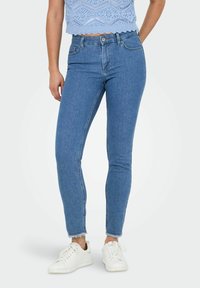 Jeans ajustados de denim azul con un dobladillo deshilachado. Combinados con zapatillas blancas y un top de punto corto en azul claro con un patrón texturizado.