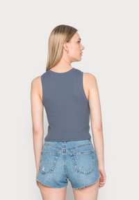 Top de alças cinza com nervuras, combinado com calções de ganga rasgados de cintura alta. O top tem um decote redondo e é sem mangas.